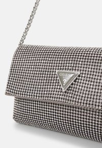 Pochette de soirée argentée recouverte de rhinestones circulaires, avec une plaque de logo triangulaire et une chaîne pour le porter.