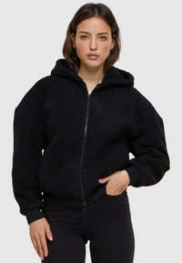 Black zip-up hoodie made of fluffy fleece material, featuring a hood, ribbed cuffs, and elastic waistband. No distinctive patterns or accents.