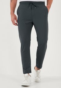 Donkergrijze sportbroek met een elastische tailleband, een trekkoord en zijzakken, gecombineerd met witte sneakers. Glad, lichtgewicht materiaal.