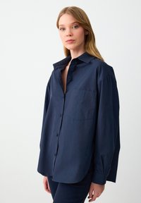 Navy blue button-up shirt, featuring a relaxed fit, long sleeves, single chest pocket, and a smooth texture.