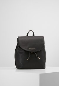 Mochila de cuero negro con una forma estructurada, tapa plegable, herrajes en tono dorado y cierre de cordón. Logo "Valentino" en el frente.