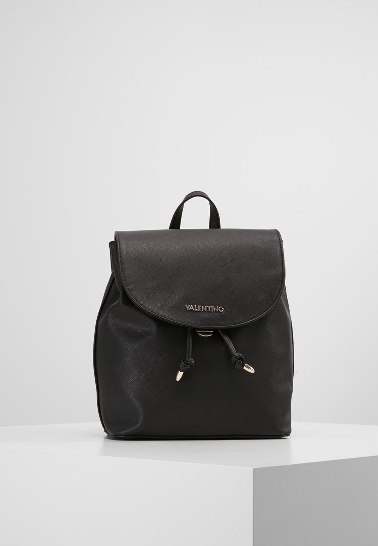Mochila de cuero negro con una forma estructurada, tapa plegable, herrajes en tono dorado y cierre de cordón. Logo "Valentino" en el frente.