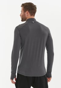 Langermige sportshirt gemaakt van lichtgewicht, grijze stof. Heeft een hoge kraag en duimopeningen bij de manchetten. Minimalistisch ontwerp.