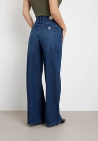 Vida jeans i mörk denim. Hög midja med två bakfickor och varumärkesetikett. Slät textur, kontrasterande sömnad och en lös passform.