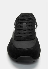 Pantofii de sport negri cu panouri din suede și plasă, șireturi negre și un design zigzag alb pe lateral, fotografiați din față.