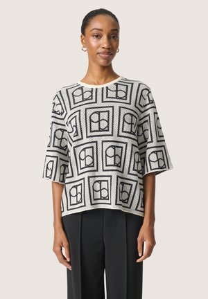 Short-sleeve knit top featuring a black and white geometric pattern, with a rounded neckline and relaxed fit. Soft texture, solid color base.