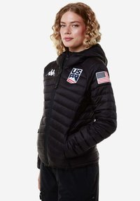 Giacca a vento nera con cappuccio, dotata di zip frontale, tasche laterali e toppa della bandiera statunitense sulla manica. Texture trapuntata distintiva e logo.