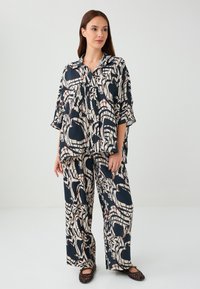 Set di abbigliamento da casa a due pezzi composto da una tunica a maniche corte e pantaloni a gamba larga. Realizzato in tessuto leggero con un motivo astratto blu navy e crema.