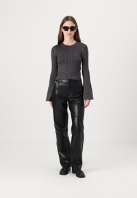 Zwarte ribbel longsleeve met uitlopende mouwen, gecombineerd met zwarte faux leren recht-pijpen broek. Model draagt donkere zonnebril en schoenen.
