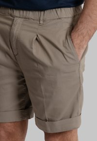 Pantaloni corti beige realizzati in tessuto leggero, dotati di una fascia elastica in vita, tasche laterali e risvolti per un fit rilassato.
