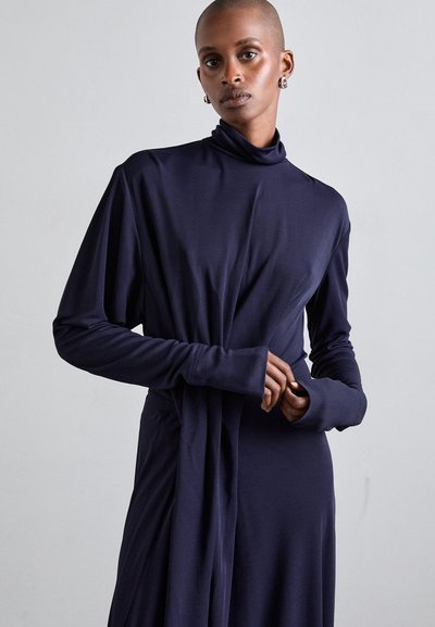 Long-sleeve, turtleneck dress in dark navy fabric. Soft, draping material with a fitted silhouette and gathered detail at the waist.