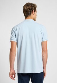 Ljusblå piké med korta ärmar, med en ribbad krage och muddar. Tyget ser slätt ut med en enkel design och inga synliga mönster.