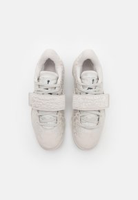 Fehér sportcipők, melyek texturált felsőrészűek, állítható pánttal és bonyolult dombornyomott mintázattal rendelkeznek. Kényelmet és rugalmasságot nyújtanak.