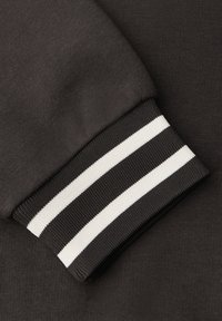 Tissu de sweat-shirt noir avec une texture, comportant un poignet avec des rayures contrastées noires et blanches pour le détail.