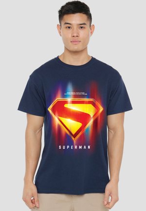 Young man wearing a navy blue T-shirt with a glowing Superman emblem and the text "Superman" below it.