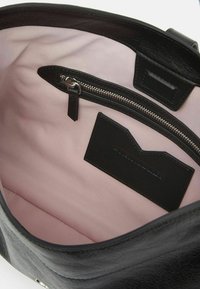 Interno di una borsa a tracolla in pelle nera con foderatura rosa chiaro, dotata di una tasca con zip e un'etichetta in pelle nera, texture liscia e forma arrotondata.