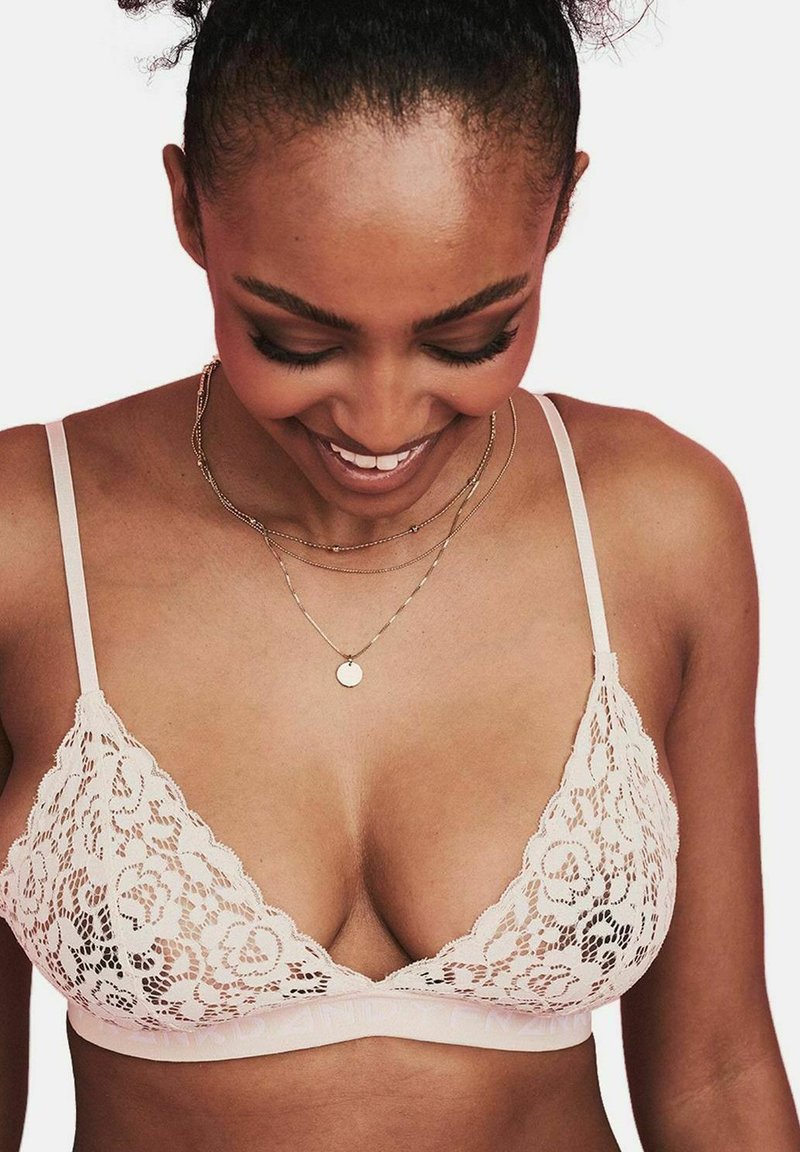 Bralette met kantafwerking in blushroze, met driehoekige cups, verstelbare bandjes en een zachte band. Heeft een bloemenkantpatroon en een gladde textuur.
