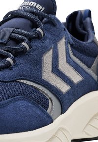 Marinblå träningsskor med överdel i mocka, nätdetaljer, grå accenter, framträdande logotyp och en texturerad gummisula.