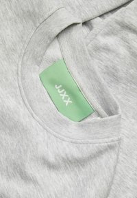 Gai pelēks T-krekls ar apaļu kakla izgriezumu. Mīksts, teksturēts kokvilnas maisījums. Zaļa birka ar baltu tekstu kakla rajonā.