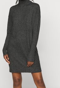 Abito lavorato a maglia grigio scuro con collo alto e maniche lunghe. Texture morbida con vestibilità ampia, che arriva a metà coscia. Design minimalista.