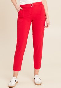 Rode slim-fit broek van een geweven stof, met zijzakken en een riem met een zilveren gesp. G gedragen met witte sneakers.