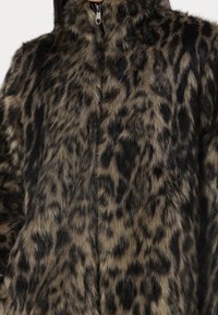 Giacca in pelliccia sintetica con stampa leopardata, dotata di un alto colletto, chiusura con zip e una superficie morbida e testurizzata in tonalità di marrone e nero.