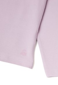 Světle fialová halenka s dlouhým rukávem, jejíž textura je žebrovaná, a má decentní vyšitý logo na lemu. Má kulatý výstřih a šité okraje.