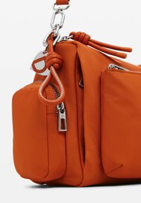 Borsa in nylon arancione con molteplici tasche con zip, una tracolla a catena grossa e notevoli accessori in metallo argentato. Finitura liscia, bordi arrotondati.