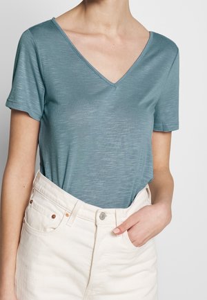 Light teal V-neck t-shirt with short sleeves, made of a soft, textured fabric. Paired with high-waisted, white denim shorts featuring visible buttons.
