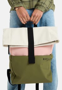 Ryggsäck med en krämfärgad rulltopp, ljusrosa mittsektion och olivgrön botten. Utrustad med svarta remmar och logodetalj. Slät textur.
