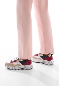 Le sneakers presentano un mix di materiali beige, rossi e navy, con una suola robusta e una scritta audace "VOILE BLANC". Indossati con pantaloni rosa chiaro.