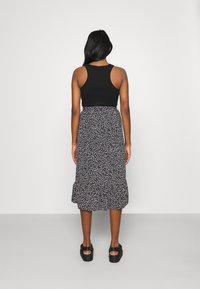 Top nero abbinato a una gonna midi con stampa floreale che presenta piccole fantasie bianche e rosa e un orlo arricciato. Scarpe nero con plateau.