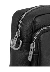 Bolso de cuero negro texturizado con doble cremallera plateada, herrajes de metal y forma rectangular. Presenta el logotipo en las tiras de las cremalleras.