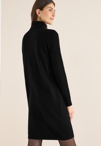 Schwarzes Strickkleid mit hohem Kragen, langen Ärmeln und geradem Schnitt. Glatte Textur und knielanger Saum. Einfaches, einfarbiges Design.
