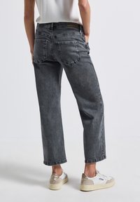 Jean droit gris foncé avec une texture délavée, deux poches arrière et une étiquette marron sur la taille. Associés à des baskets blanches.