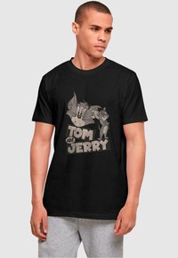 Black cotton t-shirt featuring a vintage print of cartoon characters Tom and Jerry in gray tones, with bold text reading "Tom and Jerry."
