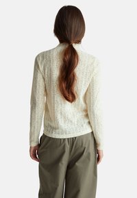 Maglione lavorato a maglia morbido di colore crema con un motivo floreale testurizzato e polsini a costine, abbinato a pantaloni larghi color oliva.