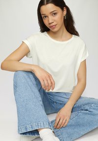 Witte korteblaasm t-shirt met een ronde hals, gedragen met lichtblauwe wijde jeans, zittende houding, soepele stofstructuur, en een minimalistisch ontwerp.