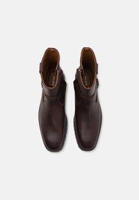 Brown leather ankle boots with a smooth finish, side zippers, and a contrasting tan interior lining. Rubber sole with subtle traction.