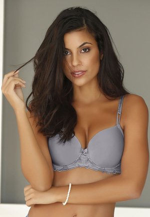 Gray padded bra with lace detailing at the base, adjustable straps, and a smooth finish. Model poses with long hair and a beaded bracelet.