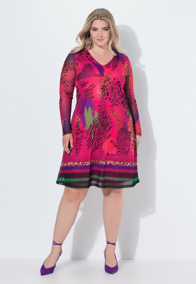 Vestido rosa vibrante con mangas largas, que presenta patrones de animales y flores, se ensancha en la cintura y tiene un dobladillo negro. Combinado con tacones morados.