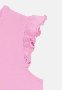 Pink sleeveless top featuring a ruffled shoulder. Made of soft fabric with a smooth texture, it includes neat stitching along the edges.