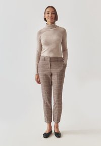 Maglione beige a collo alto abbinato a pantaloni a quadri marroni con una vestibilità slim, tasche frontali e lunghezza cropped; scarpe nere slip-on.