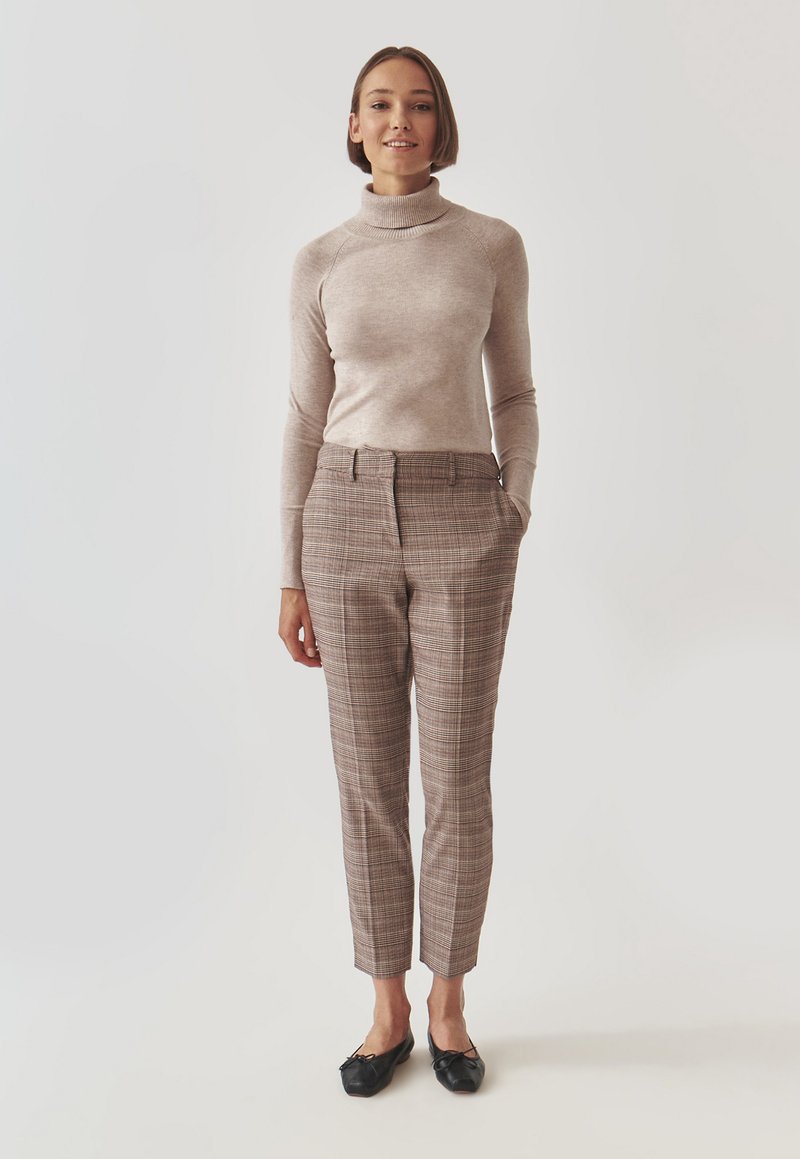 Maglione beige a collo alto abbinato a pantaloni a quadri marroni con una vestibilità slim, tasche frontali e lunghezza cropped; scarpe nere slip-on.