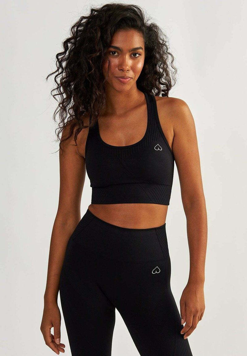 Soutien-gorge de sport noir à côtes et leggings taille haute avec un petit logo en forme de cœur. Tissu lisse et extensible avec une coupe ajustée.