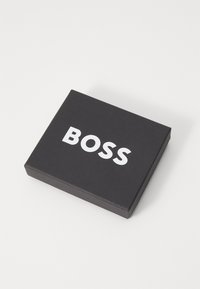 Boîte rectangulaire noire avec une finition mate, arborant un texte blanc en gras "BOSS" centré sur la surface supérieure.