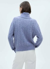 Maglione lavorato a maglia di un delicato color lavanda chiaro con collo alto a mock, caratterizzato da un motivo a treccia testurizzato e orlo a costine, abbinato a jeans bianchi.