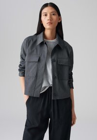 Grijs gestreepte, knopenjack met twee voorkruisen, gecombineerd met een grijze shirt en losse zwarte broek. Gladde textuur, moderne silhouette.