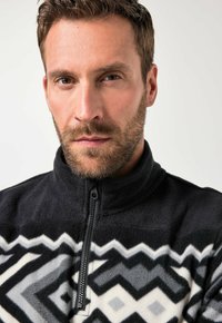 Sudadera de forro polar negra con cuello alto, que presenta un patrón geométrico en gris y blanco. Cierre con cremallera y tejido texturizado.