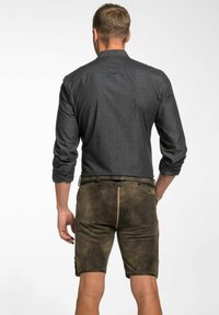 Dunkelgraues, langärmliges Hemd mit hochgekrempelten Ärmeln, kombiniert mit braunen Lederhosen. Die Shorts haben seitliche Taschen und eine strukturierte Oberfläche.